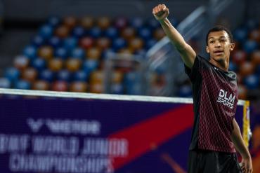 Юный игрок в тёмной форме вскинул кулак у сетки, на баннере — надпись BWF World Junior Championships (фото: BWF/Badmintonphoto — Raphael Sachetat) Юный игрок в тёмной форме вскинул кулак у сетки, на баннере — надпись BWF World Junior Championships (фото: BWF/Badmintonphoto — Raphael Sachetat)