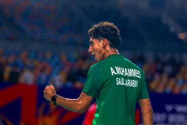 Амер Мохаммед в зелёной майке с белой надписью A.MCHAMMED и SAULARABIA сжимает кулак, на левом запястье чёрные часы, трибуны размыты (фото: BWF/Badmintonphoto — Paul Foxall) Амер Мохаммед в зелёной майке с белой надписью A.MCHAMMED и SAULARABIA сжимает кулак, на левом запястье чёрные часы, трибуны размыты (фото: BWF/Badmintonphoto — Paul Foxall)