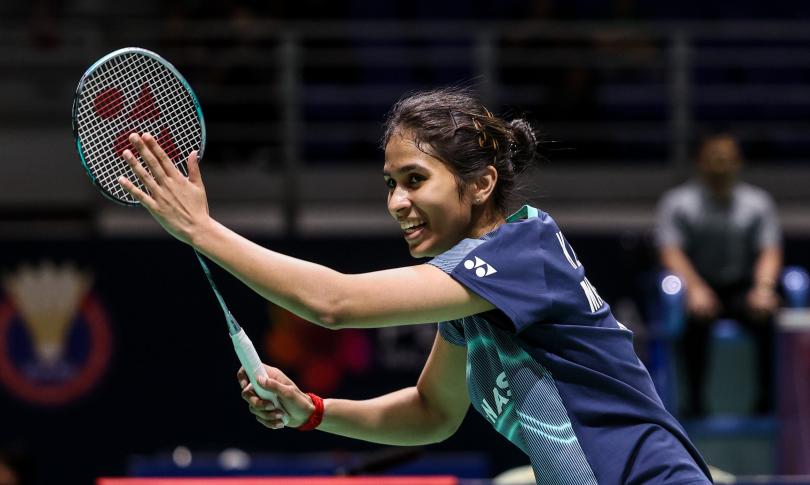 Летшанаа Карупатеван в тёмно-синей форме Yonex завершает удар с ракеткой в правой руке, на фоне размытая эмблема турнира. Фото: BWF/Badmintonphoto
