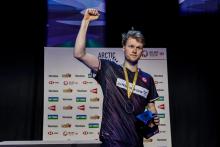 Андерс Антонсен в тёмной майке Grundfos с золотой медалью поднимает правый кулак на подиуме Arctic Open, в левой руке коробка (фото: BWF/Badmintonphoto — Yang Shaochen)