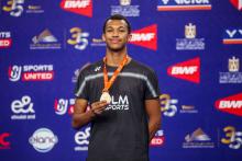 Юниор в тёмной майке LM SPORTS держит бронзовую медаль на оранжевой ленте VICTOR, за спиной баннеры BWF и герб Египта (фото: BWF/Badmintonphoto — Raphael Sachetat)